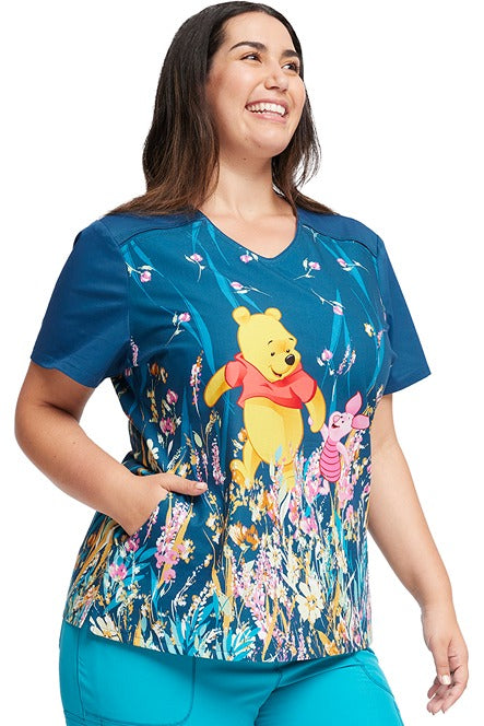 A young female CNA wearing a Tooniforms Women's V-Neck Print Top in "Flower Walk" featuring a modern classic fit & short sleeves to keep you looking & feeling cool all day long.