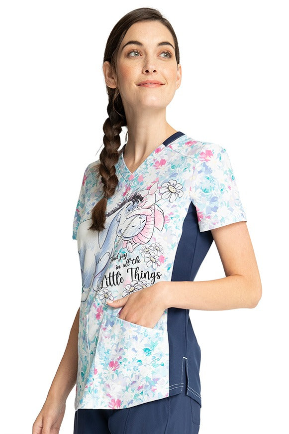 A young female CNA wearing a Cherokee Tooniforms Women's V-Neck Print Top in "Find Joy" featuring 2 front in-seam pockets.