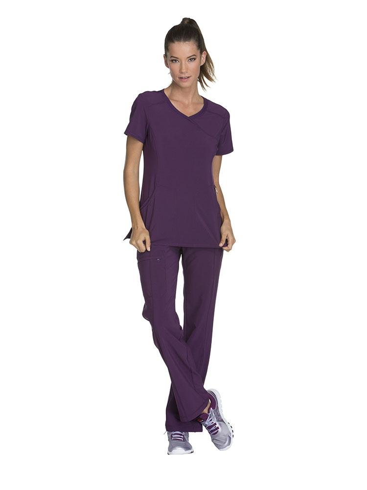 A young female Nurse wearing a Cherokee Infinity Women's Antimicrobial Mock Wrap Top in Eggplant size XS featuring a mock wrap neckline.