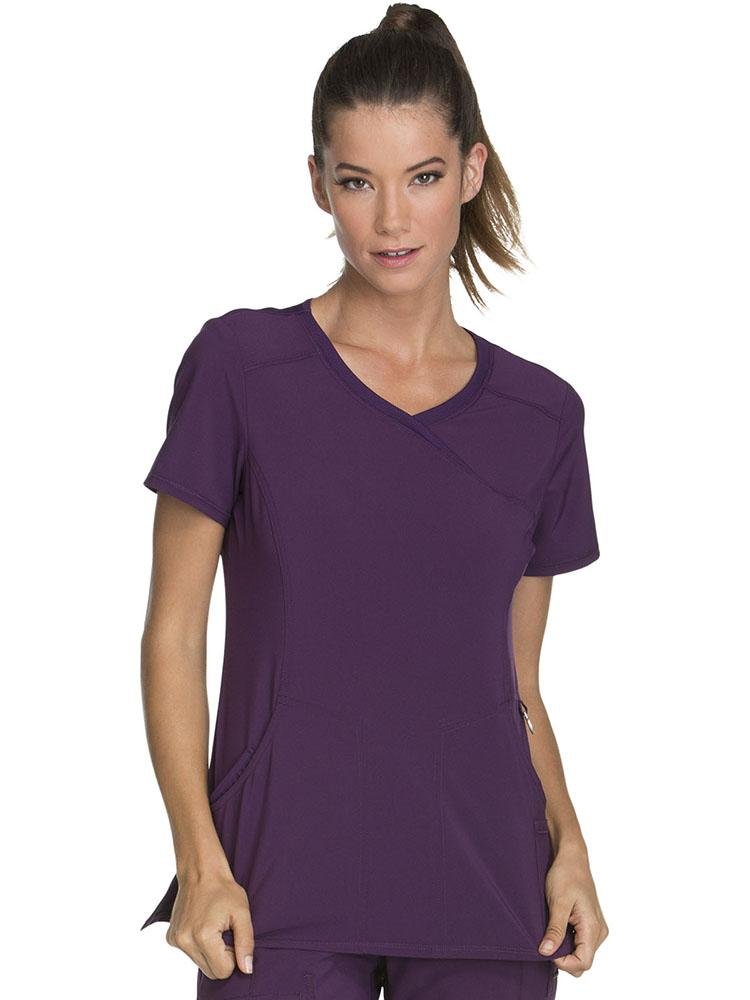 A female Clinical Laboratory Technologist wearing a Cherokee Infinity Women's Antimicrobial Mock Wrap Top in eggplant featuring a stretch back panel for additional range of motion.