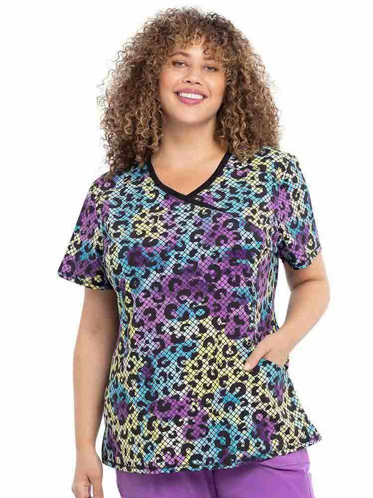 A young female Pediatric Nurse wearing an Infinity Women's Mock Wrap Printed Scrub Top in "Wild Mesh" featuring two front slash pockets.
