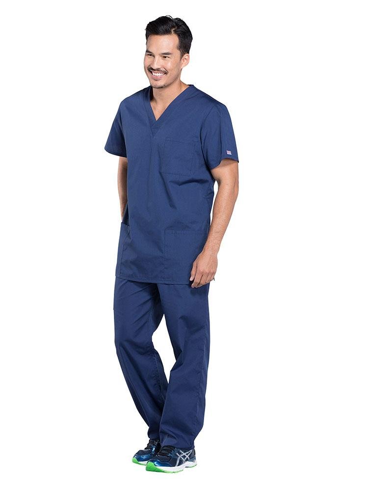 A young male Nursing Assistant wearing a Cherokee Workwear Originals Unisex Multi-Pocketed V-neck Scrub Top in Navy size XL featuring side slits for additional mobility throughout the day.