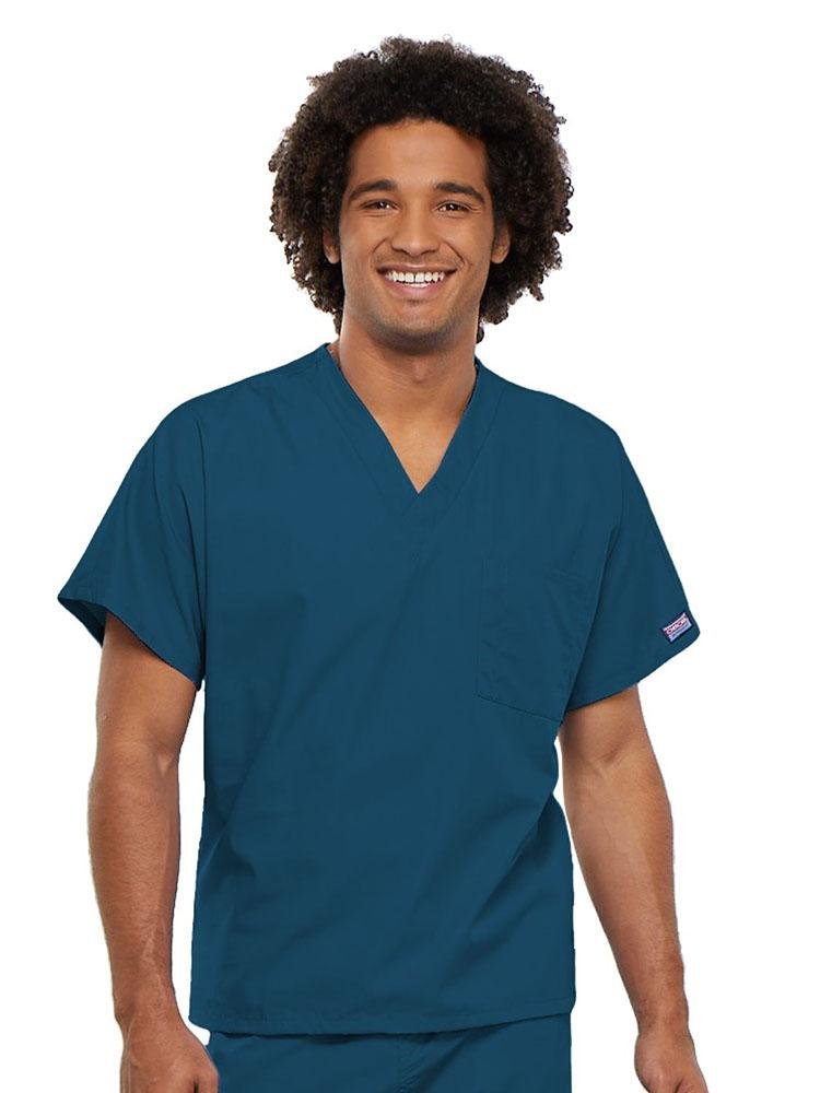 A young male Physician's Assistant wearing a Cherokee Workwear Originals Unisex Single Pocket V-neck Scrub Top in Caribbean size XL featuring short sleeves.