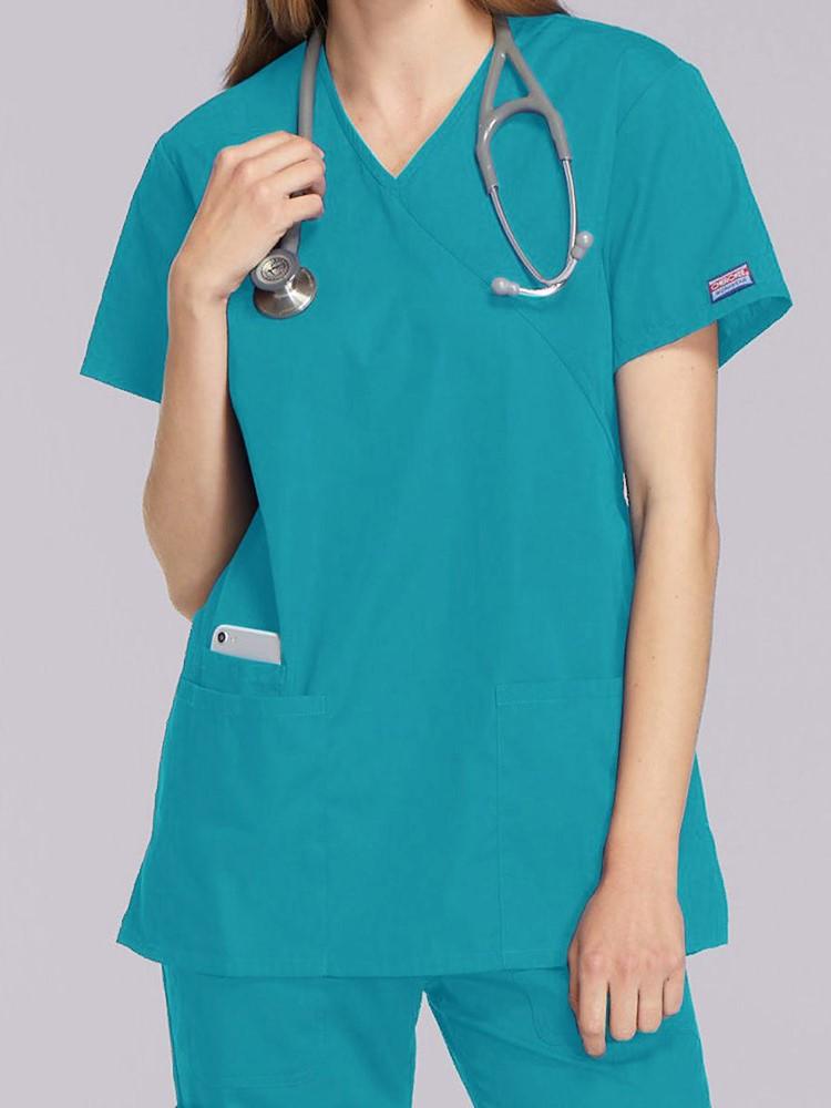 A young female EMT wearing a Cherokee Workwear Originals Women's Mock Wrap Top in Teal size 2XL featuring short sleeves.