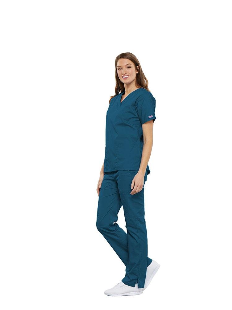 A female Clinical Laboratory Technologist wearing a Cherokee Workwear Originals women's Multi-Pocketed V-Neck Scrub Top in Caribbean size medium featuring side seam vents for additional range of motion throughout the day.