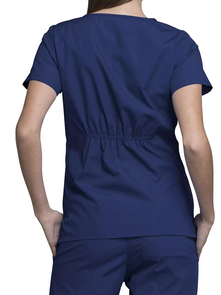 A young female Registered Nurse wearing a Cherokee Workwear Original's Women's Notch Crew Round Neck Scrub Top in Navy size Medium featuring back elastic to provide a flattering all day fit.