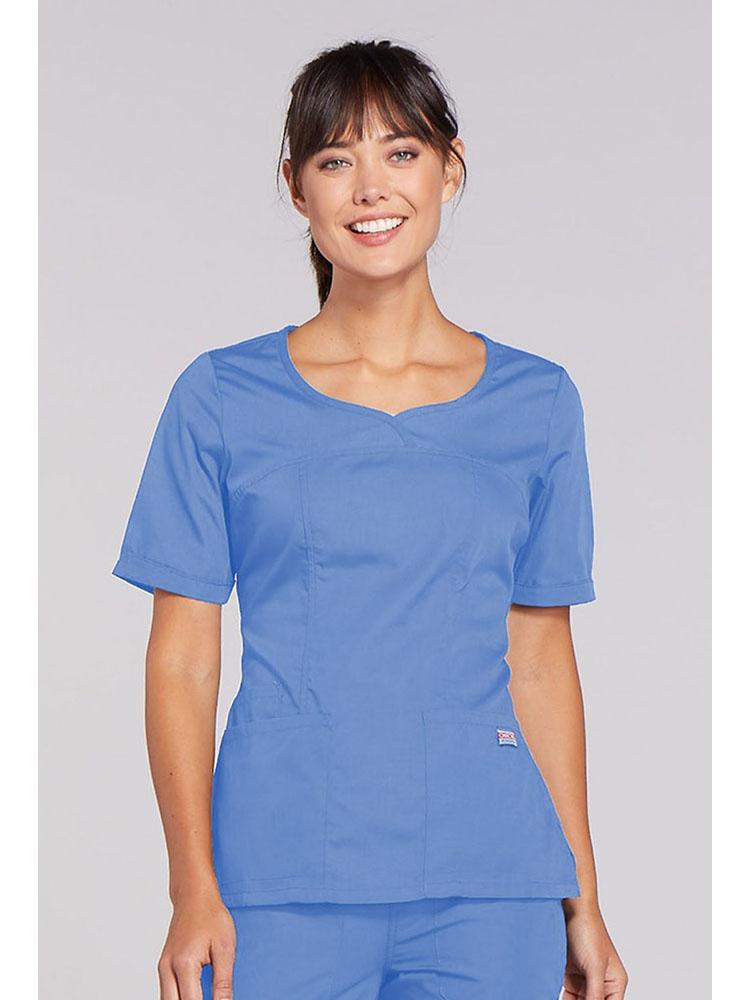 A young female Occupational Therapist wearing a Cherokee Workwear Original's Women's Novelty Crossed V-neckline Scrub Top in Ceil size 2XL.