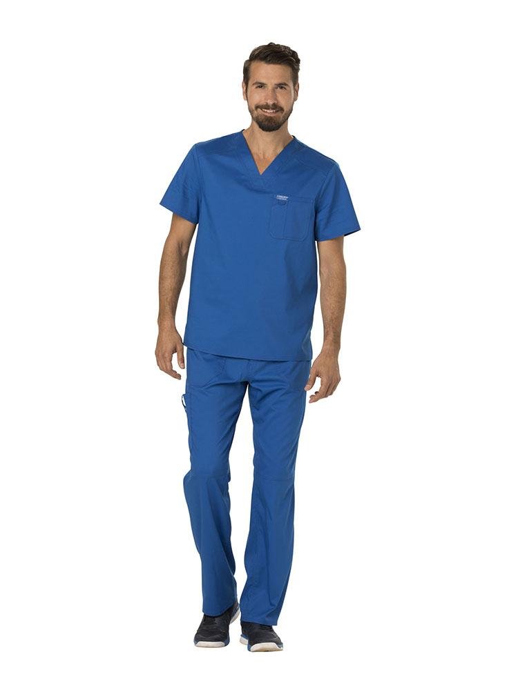 A young male Sonographer wearing a Cherokee Workwear Revolution Men's Single Pocket V-neck Scrub Top in Royal Blue size Small featuring a v-neckline & short sleeves.