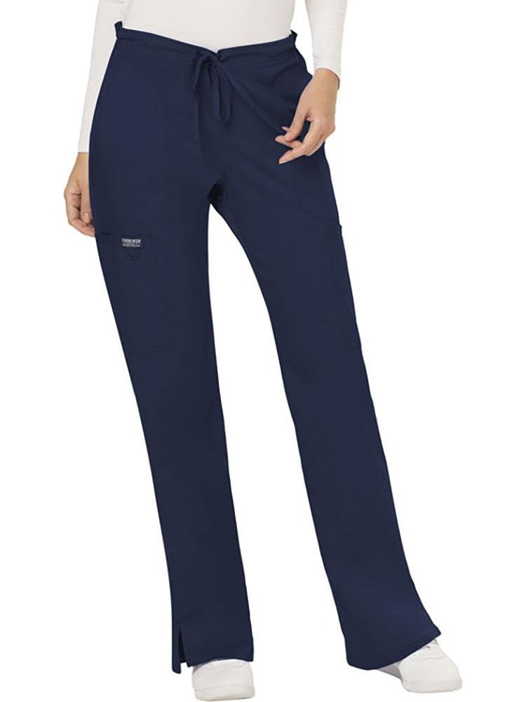 A young female Nurse wearing a Cherokee Workwear Revolution Women's Mid Rise Moderate Flare Scrub Pant in Navy size XL Petite featuring a drawstring waist to provide a flattering & comfortable all day fit.