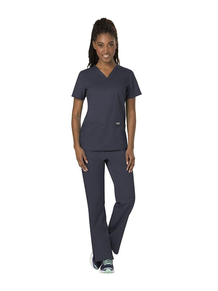 A young female Physician's Assistant wearing both the Cherokee Workwear Revolution women's V-Neck Scrub Top & Elastic Waistband Pull-On Scrub Pant in Pewter size Small.