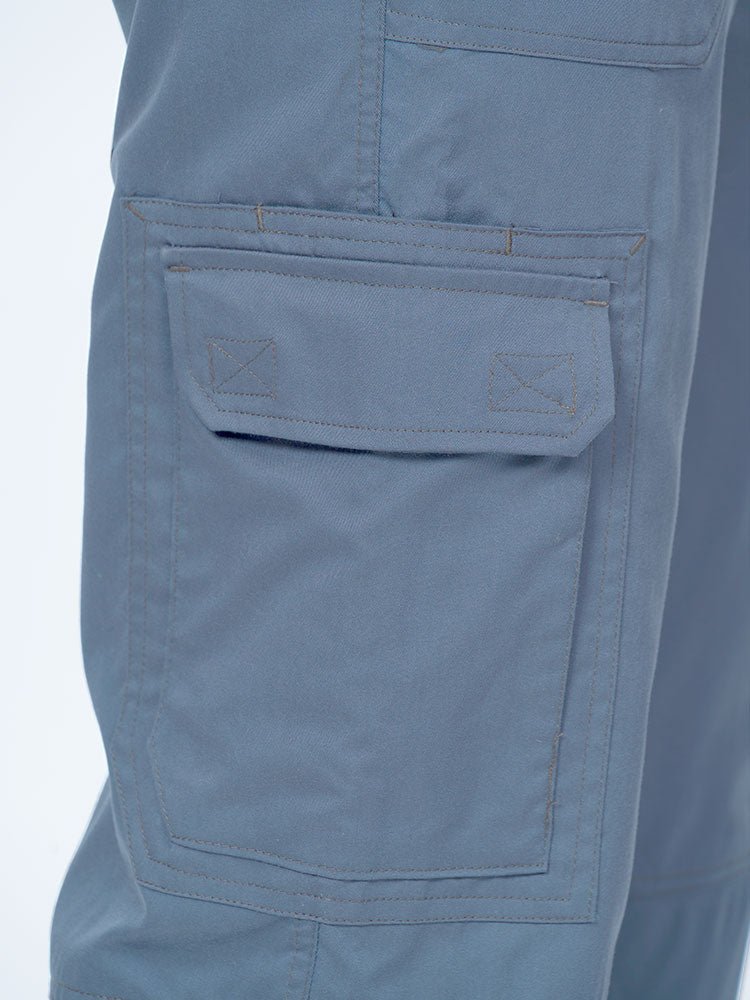 Man wearing an Epic by MedWorks Men's Button Front Scrub Pant in blue fog with 1 double cargo pocket on wearer's right side.