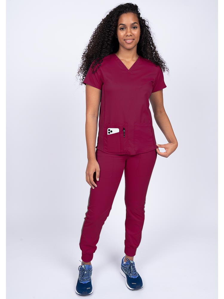Young female healthcare professional wearing an Epic by MedWorks Women's Blessed Scrub Top in wine with a total of 3 pockets & 1 pen slot.
