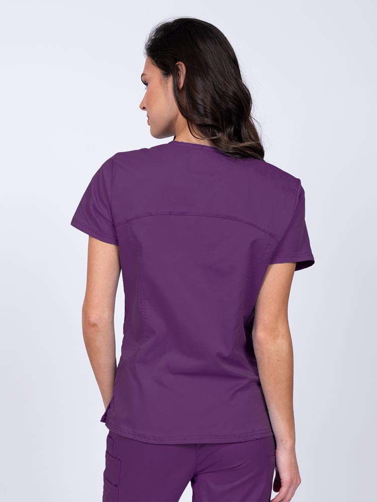 Young female nurse wearing an Epic by MedWorks Women's Knit Collar Mock Wrap Scrub Top in eggplant with stylish seaming throughout.