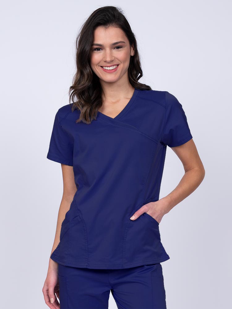 Young RN wearing an Epic by MedWorks Women's Knit Collar Mock Wrap Scrub Top in navy featuring a Y-neckline with short sleeves.