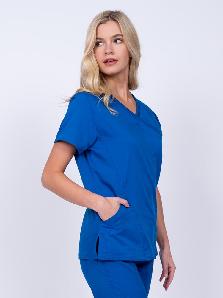 Woman wearing an Epic by MedWorks Women's Knit Collar Mock Wrap Scrub Top in royal featuring two front slash pockets.