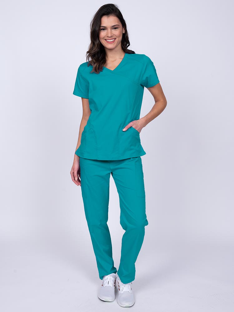 Young female healthcare worker wearing an Epic by MedWorks Women's Knit Collar Mock Wrap Scrub Top in teal featuring a 2 way stretch fabric that allows air to pass easily through the garment.