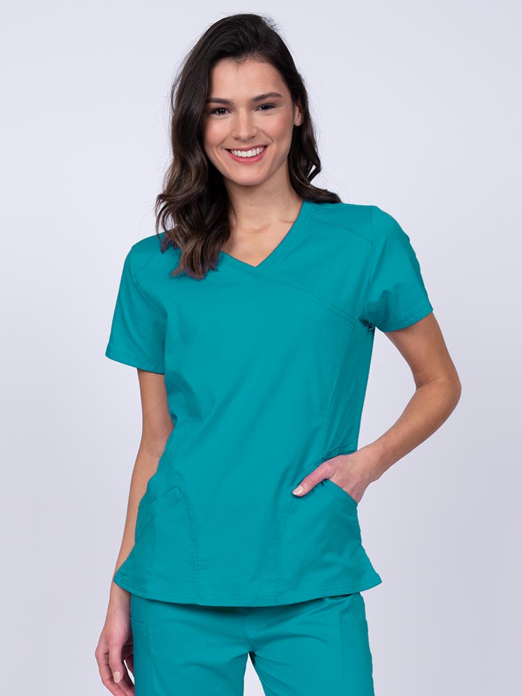 Young RN wearing an Epic by MedWorks Women's Knit Collar Mock Wrap Scrub Top in teal featuring a Y-neckline with short sleeves.