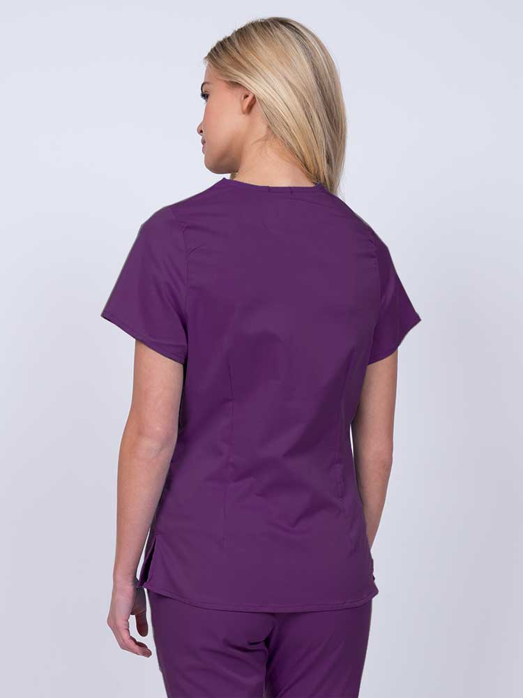 Nurse wearing an Epic by MedWorks Women's Mock Wrap Scrub Top in eggplant with side slits for additional range of motion.