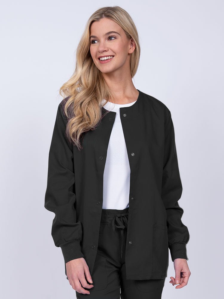 Young female healthcare worker wearing an Epic by MedWorks Women's Snap Front Scrub Jacket in black with two front patch pockets.