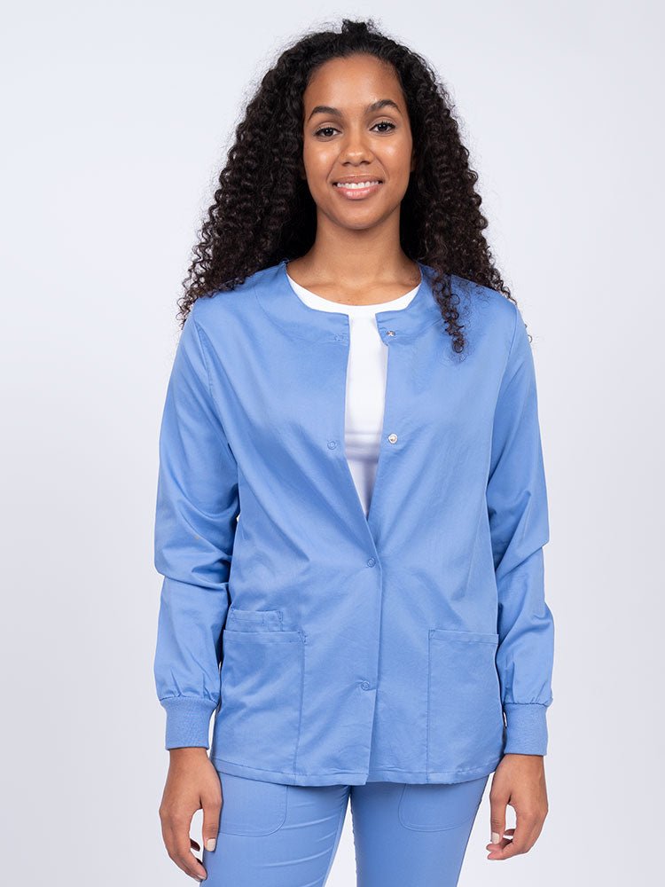 Young female healthcare worker wearing an Epic by MedWorks Women's Snap Front Scrub Jacket in ceil with two front patch pockets.