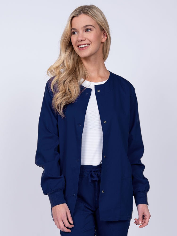 Young female healthcare worker wearing an Epic by MedWorks Women's Snap Front Scrub Jacket in navy with two front patch pockets.