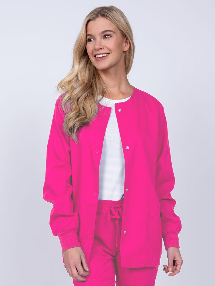 Young female healthcare worker wearing an Epic by MedWorks Women's Snap Front Scrub Jacket in shocking pink with two front patch pockets.