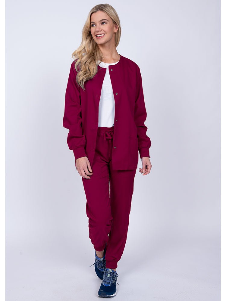 Woman wearing an Epic by MedWorks Women's Snap Front Scrub Jacket in wine with rib knit cuffs.