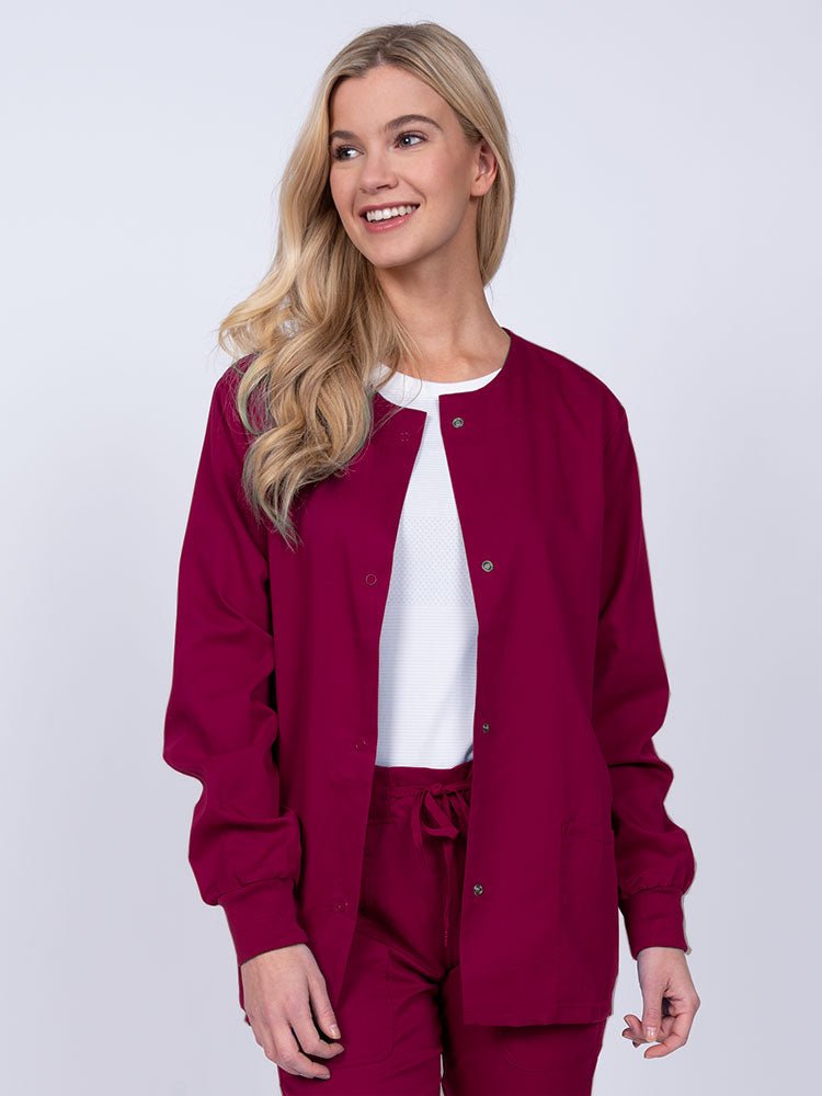 Young female healthcare worker wearing an Epic by MedWorks Women's Snap Front Scrub Jacket in wine with two front patch pockets.