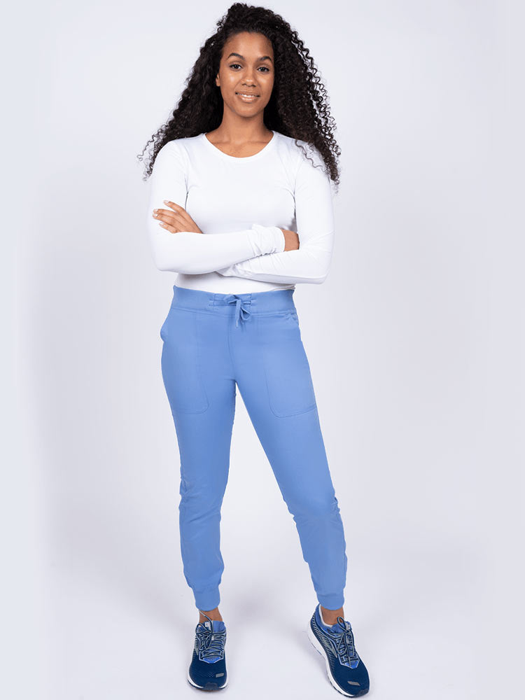 A young lady nurse wearing an Epic by MedWorks Women's Yoga Jogger Scrub Pant in Ceil size Large Petite featuring stylish cover stitch detail throughout.
