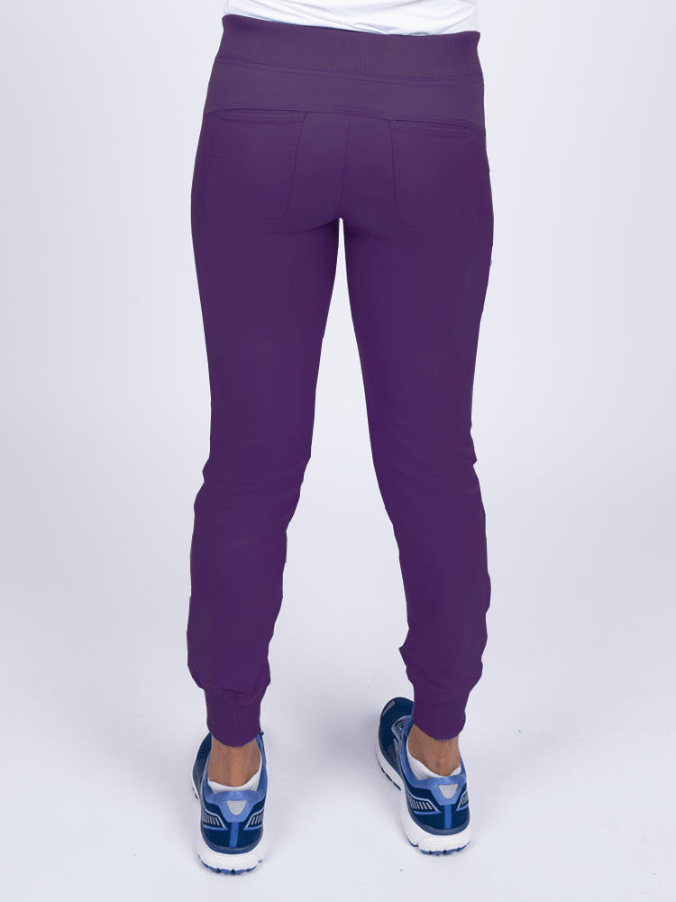 A young female Nurse Practitioner wearing an Epic by MedWorks Women's Yoga Jogger Scrub Pant in Eggplant size small featuring 2 back patch pockets.