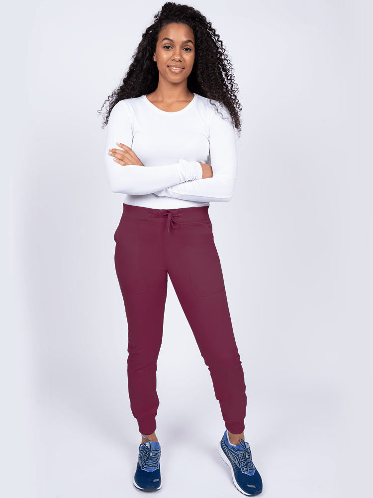 A young lady nurse wearing an Epic by MedWorks Women's Yoga Jogger Scrub Pant in Wine size Large Petite featuring stylish cover stitch detail throughout.