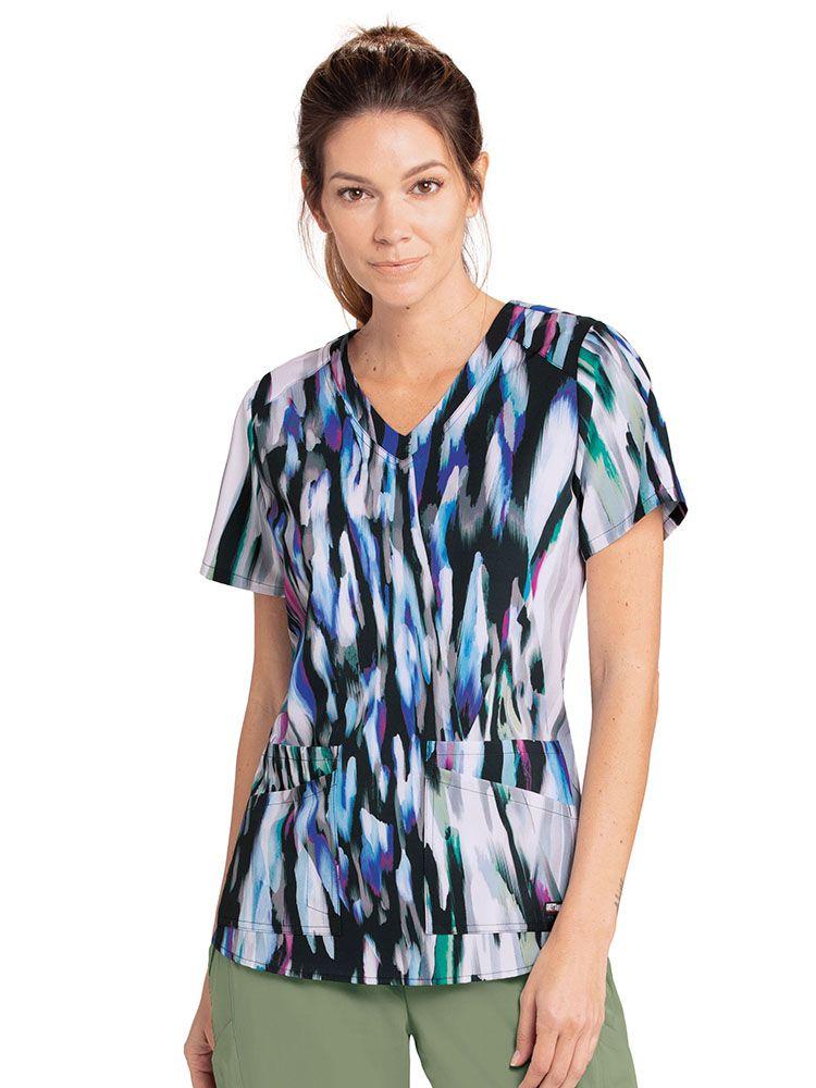 A young female Pediatric Nurse wearing a Grey's Anatomy Women's Casey Printed Scrub Top in "Silver Cascades" featuring 4 front pockets.