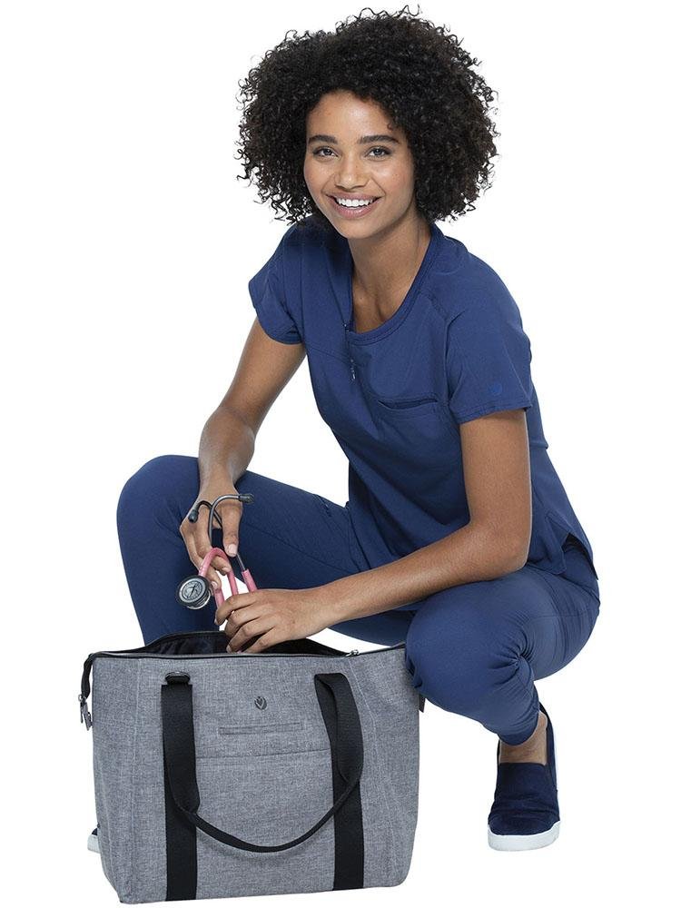 A young female Nurse Practitioner wearing Navy scrubs placing a stethoscope in a HeartSoul Madison Duffel Bag in Heather Grey.