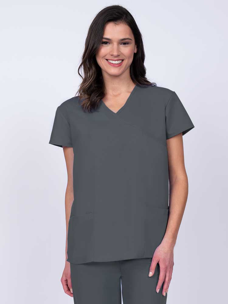 Young woman wearing a Luv Scrubs by MedWorks Women's Mock Wrap Scrub Top in pewter featuring a Y-neckline and side slits for additional range of motion.