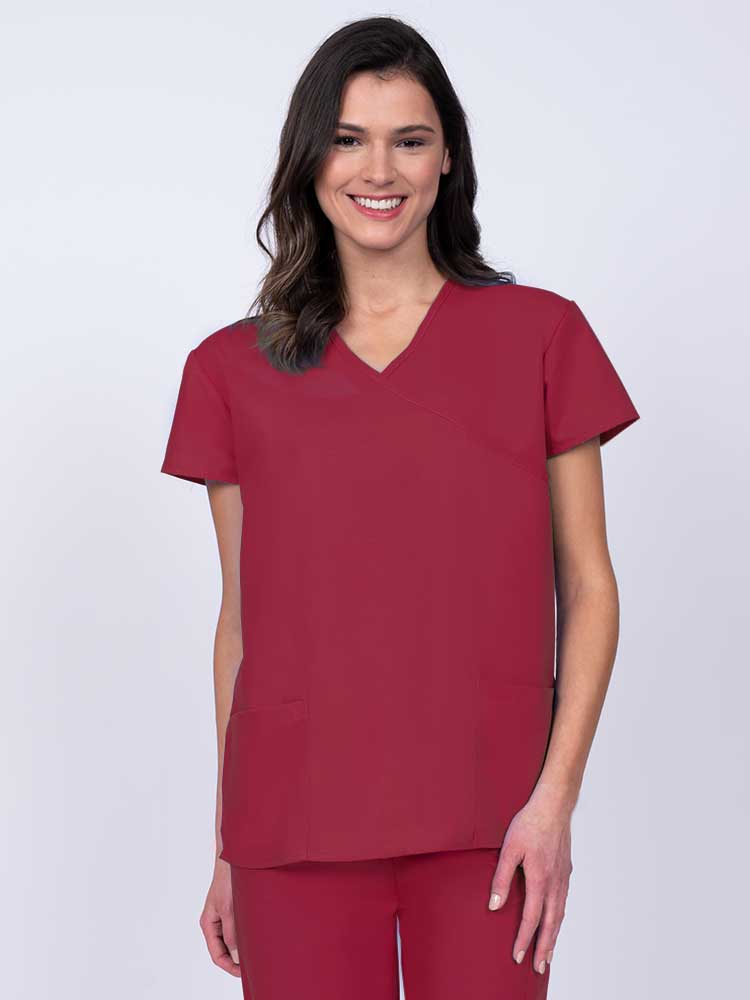 Young woman wearing a Luv Scrubs by MedWorks Women's Mock Wrap Scrub Top in red featuring a Y-neckline and side slits for additional range of motion.