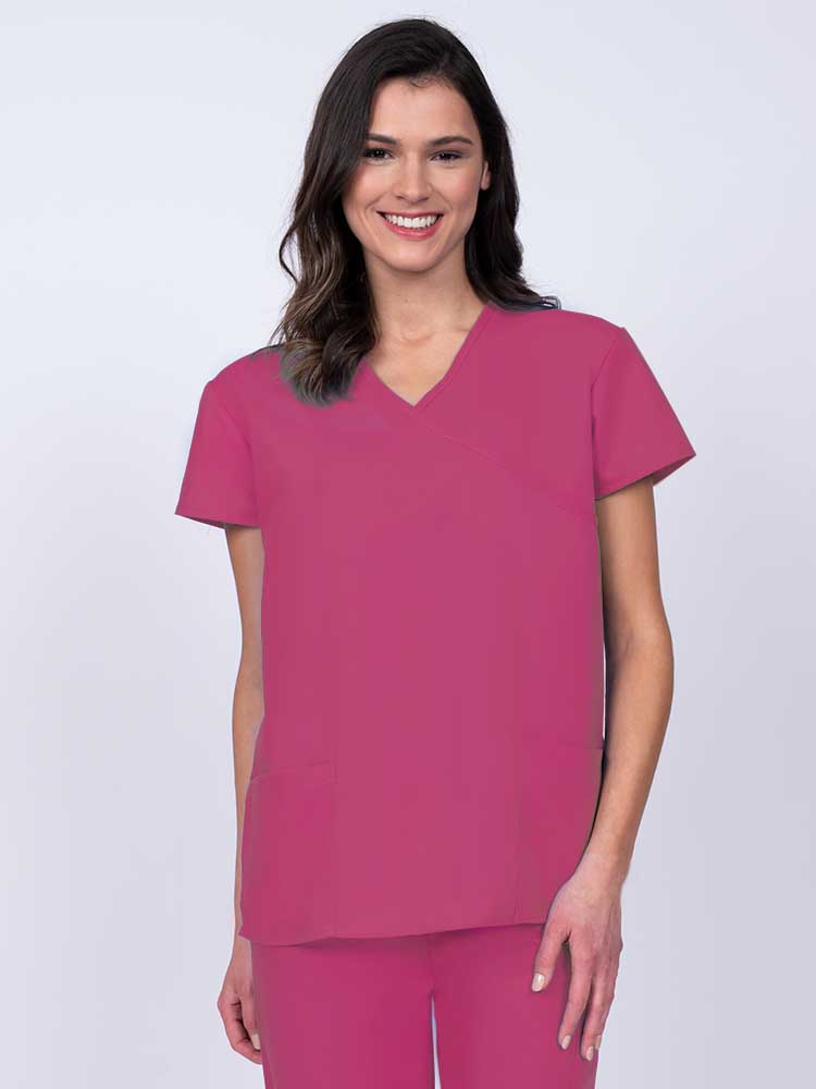 Young woman wearing a Luv Scrubs by MedWorks Women's Mock Wrap Scrub Top in shocking pink featuring a Y-neckline and side slits for additional range of motion.