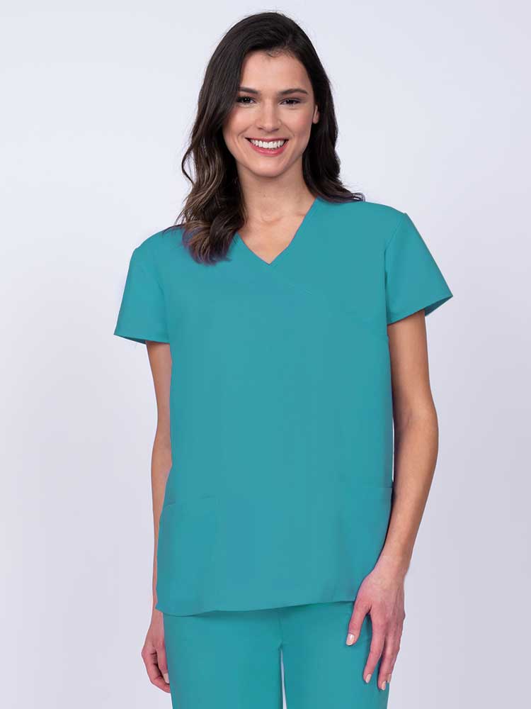 Young woman wearing a Luv Scrubs by MedWorks Women's Mock Wrap Scrub Top in turquoise featuring a Y-neckline and side slits for additional range of motion.