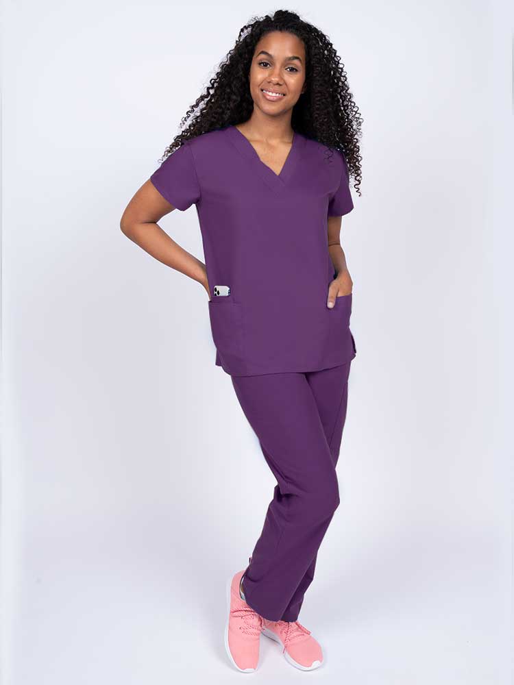 Woman wearing a Luv Scrubs by MedWorks Women's V-neck Scrub Top in eggplant with 2 front patch pockets.