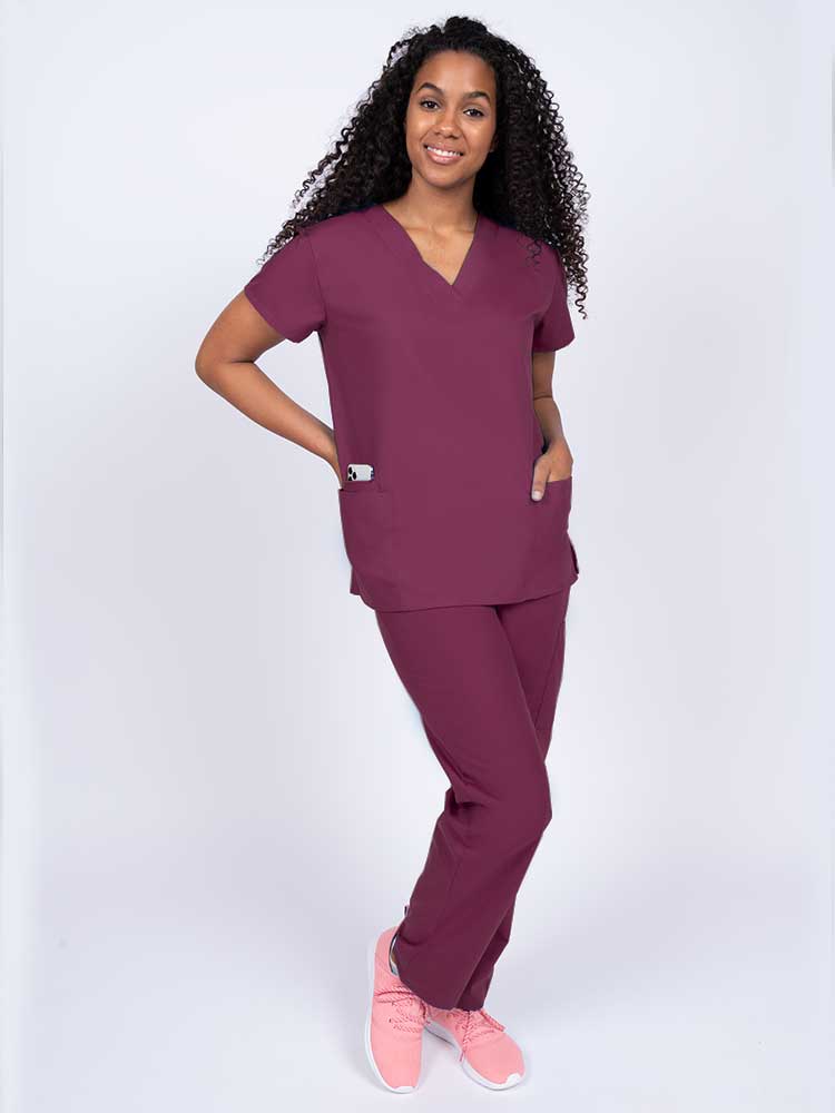 A young female Surgical Assistant wearing a Luv Scrubs by MedWorks Women's V-neck Scrub Top in Wine size XL featuring a classic fit for a roomy and relaxed all day fit.