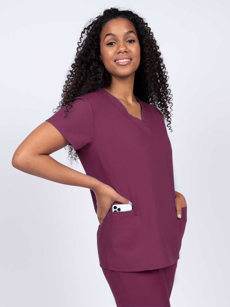A young female surgeon wearing a Luv Scrub by MedWorks Women's V-Neck Scrub Top in Wine featuring 2 front patch pockets.