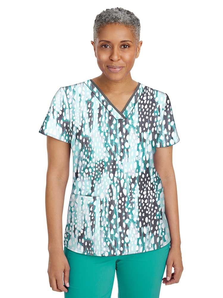 A young female Pediatric Nurse wearing a Women's Amanda Printed Scrub Top from Oremiere by Healing Hands in "Crystal Droplets" size Small featuring a V-neckline with contrast binding.