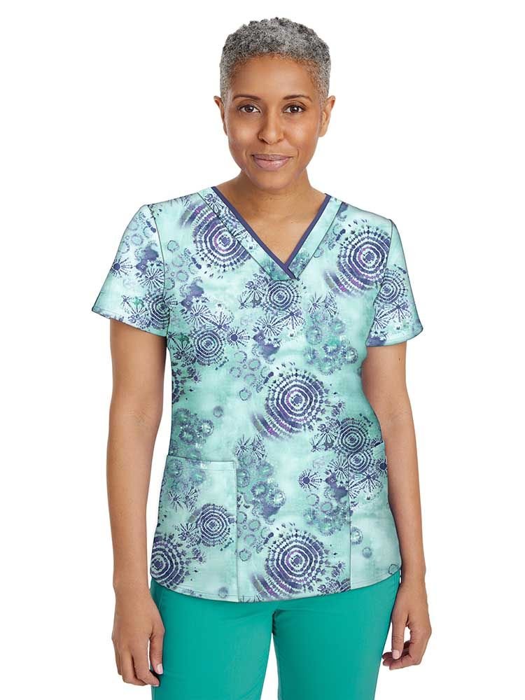 A middle aged female Pediatric Nurse wearing a Women's Amanda Printed Scrub Top from Healing Hands in "Hand Tie-Dyed" size large featuring a v-neckline and short sleeves.