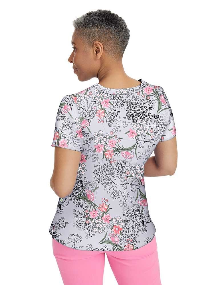 A middle aged female Pediatric Nurse wearing a Women's Amanda Printed Scrub Top from Premiere by Healing Hands featuring back shaping darts and a curved hem.