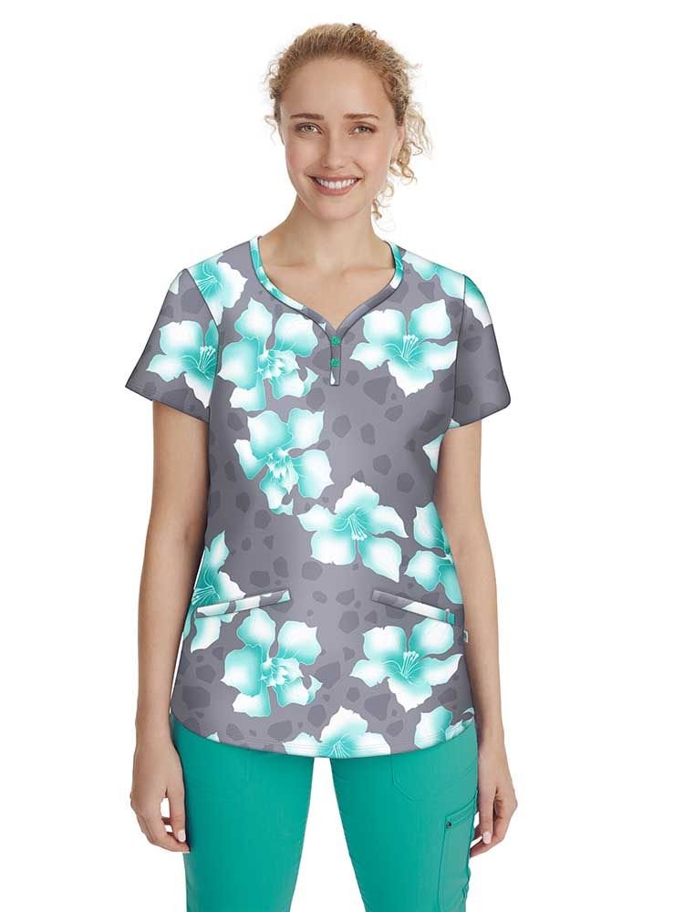 A young female pediatric nurse wearing a Women's Isabel Printed Scrub Top from Premiere by Healing Hands in "Large Blossom" featuring two front angled pockets.