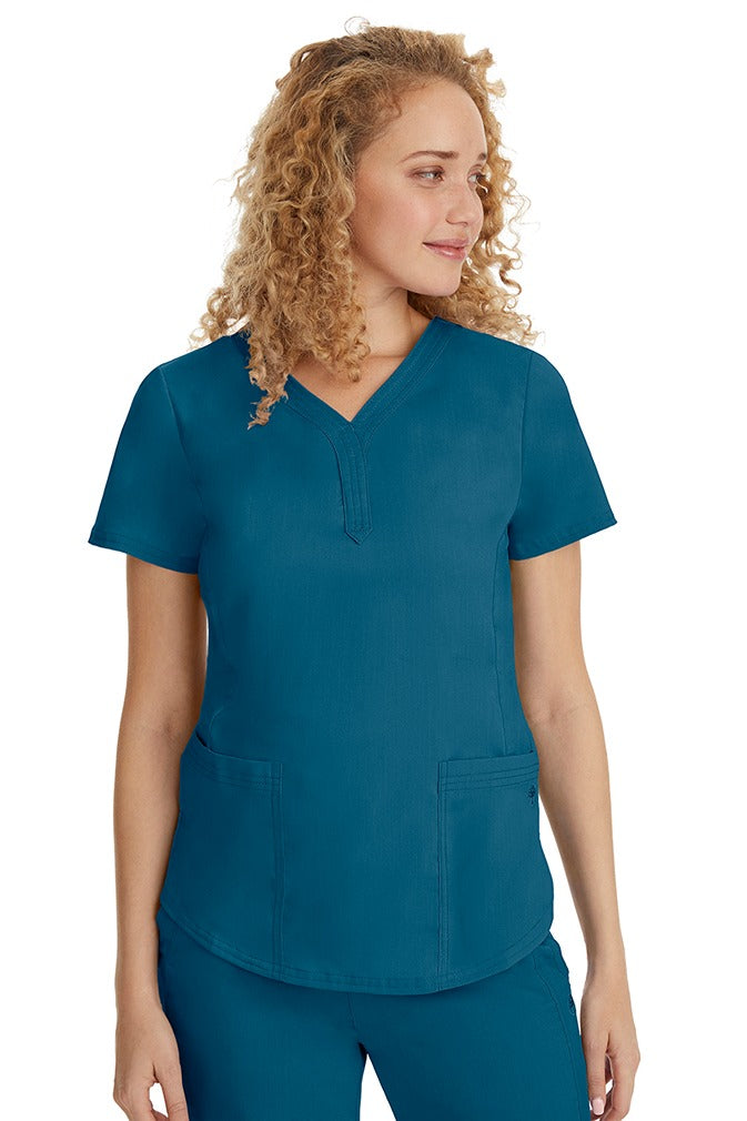 A young female healthcare professional wearing a Purple Label Women's Jane V-Neck Scrub Top in Caribbean featuring 2 front patch pockets.