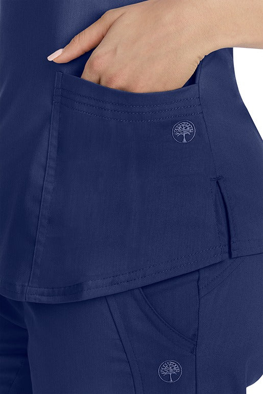 A female healthcare worker wearing a Purple Label Women's Jane V-Neck Scrub Top in Navy featuring triple needle stitch detail at the pockets.