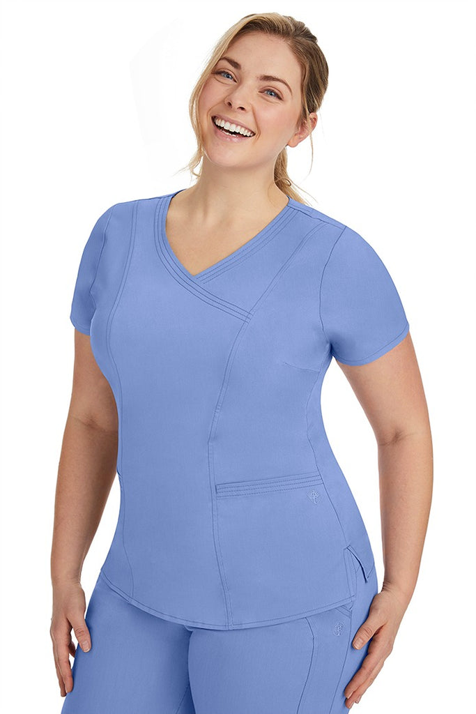 A frontward facing image of a young woman wearing a Purple Label Women's Jordan Crossover Scrub Top in Ceil featuring front darts.