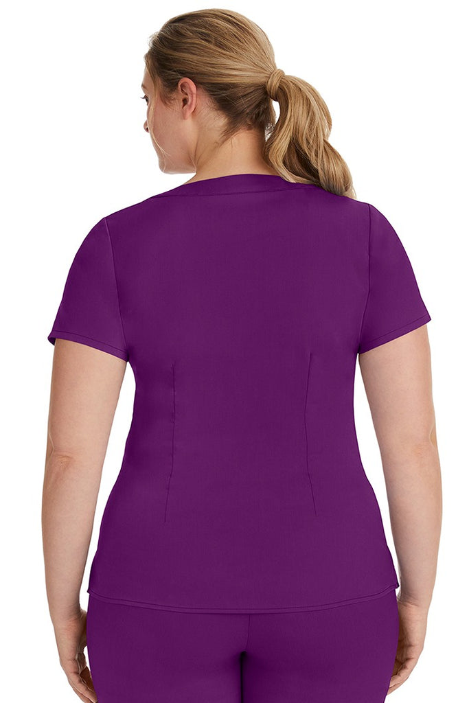 A female LPN wearing a Purple Label Women's Jordan Crossover Scrub Top in Eggplant featuring a unique stretch fabric made of 80% polyester/17% rayon/3% spandex.