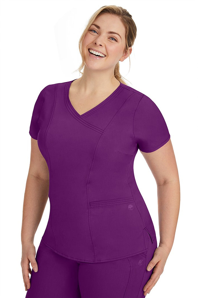 A frontward facing image of a young woman wearing a Purple Label Women's Jordan Crossover Scrub Top in Eggplant featuring front darts.