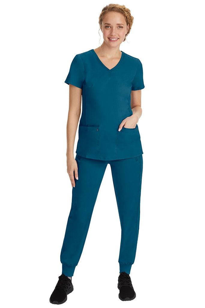 A young female nurse wearing a Purple Label Women's Juliet Yoga Scrub Top by Healing Hands in Caribbean featuring a v-neckline.